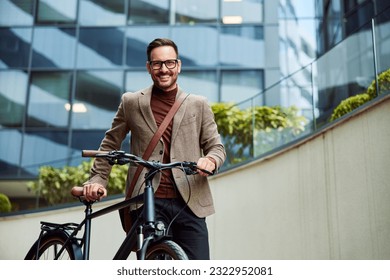 Un empresario exitoso con anteojos para empujar una bicicleta y volver a casa del trabajo, sonriendo para la cámara.