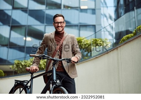 A successful businessman with glasses on pushing a bicycle and going home from work, smiling for the camera.