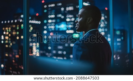 Successful Businessman Looking Out of the Window on Late Evening. Modern Hedge Fund Investor Enjoying Successful Life. Urban View with Down Town Street with Skyscrapers at Night with Neon Lights.