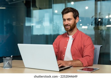 Successful businessman in red shirt happily working with laptop inside office, mature man with beard at workplace typing on keyboard smiling satisfied with work results and achievement. - Powered by Shutterstock