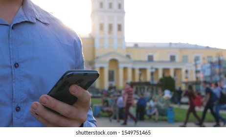 Successful Businessman In Shirt Standing Among City Street And Browsing Smartphone. Confident Man Typing Text Or Using App On His Phone. Bright Sunlight And Cityscape At Background. Slow Mo Dolly Shot