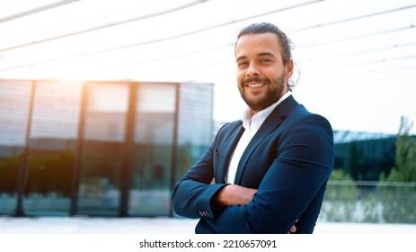 Successful Businessman Suit With Beard Standing In Front Of Office Glass Building Arm Crossed Confidently Looking In Camera And Smile. Hispanic Male Business Person Portrait. Web Banner, Free Space