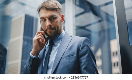 Successful Businessman In A Suit Riding Glass Elevator To Office In Modern Business Center. Handsome Serious Man Talking On A Phone, Taking An Important Business Call In A Lift.