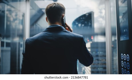 Successful Businessman In A Suit Riding Glass Elevator To Office In Modern Business Center. Handsome Happy Man Talking On A Phone, Taking An Important Business Call In A Lift