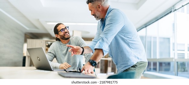 Successful businessmen smiling happily while working together in a co-working office. Two cheerful businessmen using a laptop while working on a new project. - Shutterstock ID 2187981775