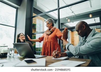 Successful Businesspeople High Fiving Each Other During A Meeting In An Office. Cheerful Business Colleagues Celebrating Their Achievement. Businesspeople Working As A Team In A Creative Workplace.