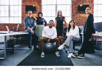 Successful businesspeople smiling at the camera in a modern office. Happy colleagues grouped together in a creative workplace. Diverse team of businesspeople looking cheerful. - Shutterstock ID 2115021884