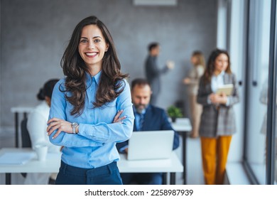 Successful businesswoman standing in creative office and looking at camera. Young woman entrepreneur in a coworking space smiling. Portrait of beautiful business woman standing in front of team - Shutterstock ID 2258987939
