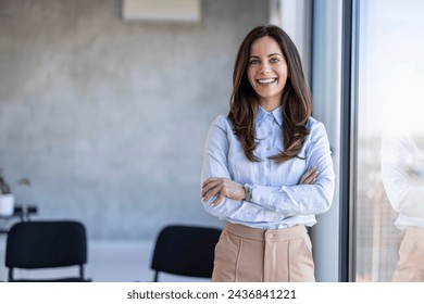 Successful businesswoman standing in creative office and looking at camera. Young woman entrepreneur in a coworking space smiling. Portrait of beautiful business woman standing - Powered by Shutterstock