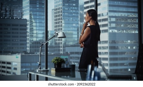 Successful Businesswoman in Stylish Dress Looking out of the Window at Big City in Downtown Area. Confident Female CEO Working on Financial Projects. Manager at Work Planning Marketing Campaign. - Shutterstock ID 2092362022
