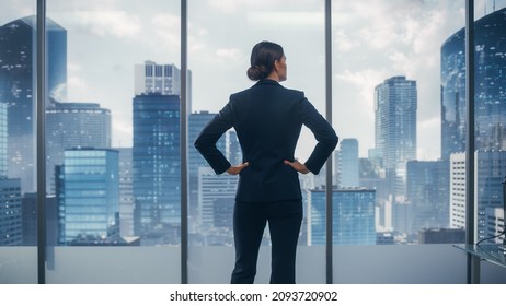 Successful Businesswoman in Stylish Suit Looking out of the Window at Big City in Downtown Area. Confident Female CEO Working on Financial Projects. Real Estate Agent Planning a Development Deal.