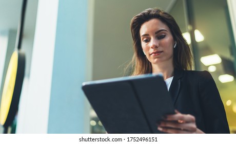 Successful businesswoman using tablet and wireless earphones outdoors near his office background lights, portrait young woman professional manager working on pc computer near window skyscraper  - Shutterstock ID 1752496151