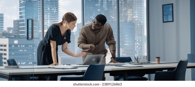 Successful Businesswoman Working on Top Floor Office Overlooking Big City. Female CEO of Humanitarian Investment Fund Talks To Black Male Investor And Discuss Graphs On Laptop.
