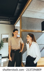 Successful businesswomen sharing a laugh in the office. Two young female entrepreneurs laughing cheerfully while standing together in a modern workspace. - Shutterstock ID 2137296809