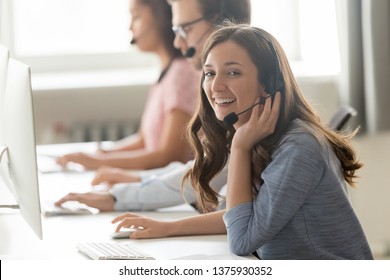 Successful call center professional telemarketing representative portrait concept. Service phone operator woman works with associates sitting on shared desk wears headset use computer looks at camera - Powered by Shutterstock