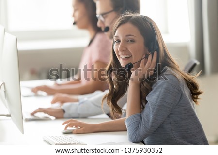 Successful call center professional telemarketing representative portrait concept. Service phone operator woman works with associates sitting on shared desk wears headset use computer looks at camera