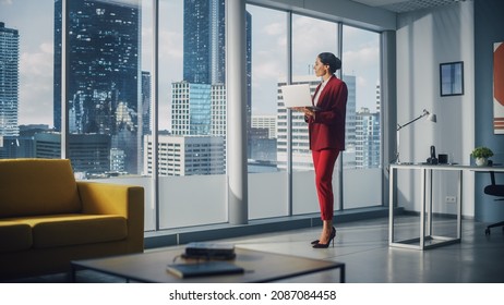Successful Caucasian Businesswoman Using Laptop While Standing in Office Looking out of Window on Big City. Confident Female Corporate CEO Managing Company Investment Strategy.
