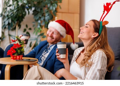 Successful Cheerful Young Business People Having Fun Celebrating Christmas At The Office, Wearing Costume Reindeer Antlers And Santa Hat, Taking A Coffee Break And Relaxing