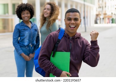 Successful Cheering Latin American Male Student With Backpack And Group Of International Students Outdoor In Summer In City