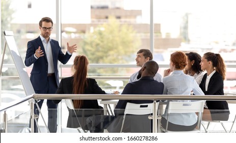Successful coach businessman presenting new project to employee. White man training and sales product to client at conference meeting room, team leader talk with diverse colleagues.
