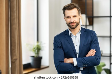 Successful confident young bearded brunet adult male entrepreneur businessman professional in business casual clothes standing with arms crossed folded at the modern home office and looking at camera - Powered by Shutterstock