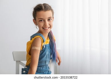 Successful Covid-19 Vaccination Concept. Vaccinated Smiling Teenage Girl Showing Arm With Adhesive Bandage After Injection, Posing Sitting At Clinic Hospital, Blurred Background, Free Copy Space