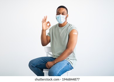 Successful Covid-19 Vaccination. Vaccinated Black Man Gesturing Okay And Showing Arm With Adhesive Bandage After Vaccine Injection, Posing Wearing Antiviral Protective Face Mask, White Background - Powered by Shutterstock