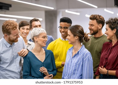 Successful creative group of casual business people talking to each other in modern office. Happy multiethnic businessmen and businesswomen standing as a team and laughing together in co-working space