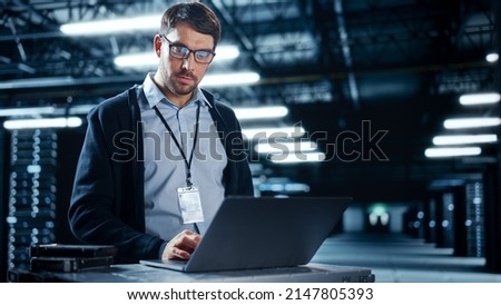 Successful Data Center IT Specialist Using Laptop Computer. Server Farm Cloud Computing Facility with System Administrator Working. Data Protection Engineering Network for Cyber Security.