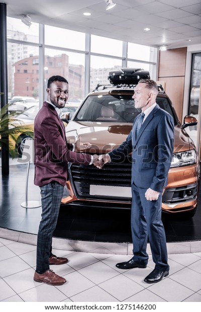Successful deal. African-American\
handsome representative of car salon smiling after successful\
deal