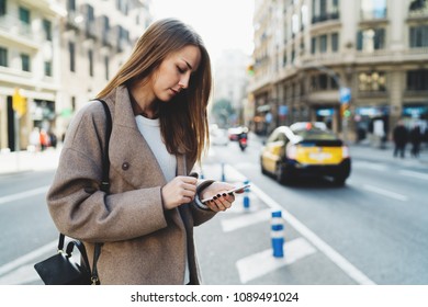 Successful designer reading email on  mobile phone connected to wifi while walking the street. Charming student girl wearing stylish clothes searching information in the internet on a smartphone.