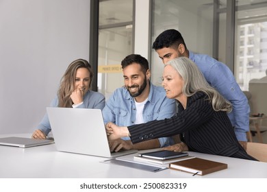 Successful diverse group of business colleagues focused on laptop watching online content, project presentation, pointing at screen, smiling, laughing, sitting at office meeting table - Powered by Shutterstock