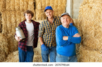 Successful Elderly Dairy Farm Owner With Adult Son And Teen Grandson Standing Together Near Straw Stack In Hayloft After Work