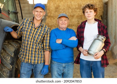 Successful Elderly Dairy Farm Owner With Adult Son And Teen Grandson Standing Together Near Straw Stack In Hayloft After Work