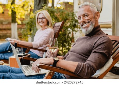 Successful elderly married couple resting on the deck chairs on the porch of their camper van with food and wine. Celebration of anniversary in traveling by trailer, on a trip by caravan home - Powered by Shutterstock