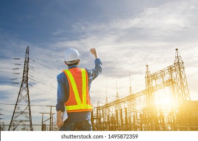 Successful engineer standing at the power substation against the sunrise background.