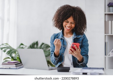 Successful And Exciting African American Businesswoman Young Woman Excited To Win On Her Smartphone At Work.