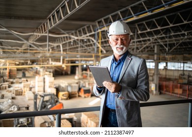 Successful factory manager or CEO holding tablet computer and checking production results in industrial plant while workers and forklifts working in background. - Shutterstock ID 2112387497