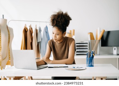 Successful fashion designer. Attractive young asian woman with smile while standing in workshop. Beautiful owner business woman working and holds tablet, laptop and smartphone on desk in studio. - Powered by Shutterstock