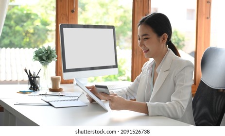 A successful female business owner or executive manager sitting at her office desk and transferring money via online application. credit card concept.