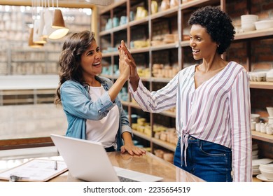 Successful female ceramists high fiving each other in their store. Two happy shop owners celebrating their achievement as a team. Cheerful young businesswomen running a creative small business. - Powered by Shutterstock