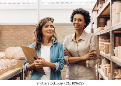 Successful female ceramists smiling at the camera in their store. Two happy businesswomen managing a store with handmade ceramic products. Young female entrepreneurs running a creative small business.
