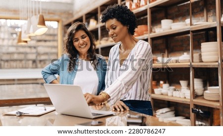 Successful female ceramists using a laptop while working together. Two female entrepreneurs managing online orders in their store. Happy young businesswomen running a creative small business together.