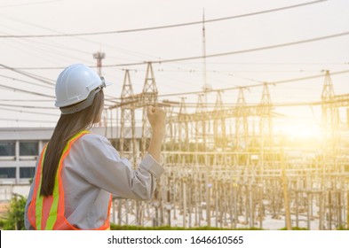 Successful Female Engineer Standing At The Power Substation Against The Sunrise Background.