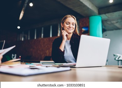 Successful female grapic designer watching tutorial about creative ideas at laptop computer during working process in office.Positive student with blonde hair reading business news on netbook - Shutterstock ID 1033103851