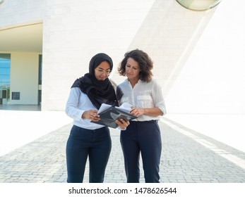 Successful Female Professionals Reviewing Documents Reports. Arab And Caucasian Business Women Standing And Reading Papers Together. Reports Concept