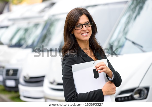 Successful female sales\
representative in van transport trade fair. Commercial exhibition\
and rental vehicle concept. Beautiful female seller or salesman\
holding car keys.