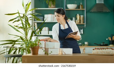 Successful Female Small Business Owner Prepares A Customer Order. Modern Designer Kitchen. Confectionery And Favorite Business. Organization Of Work In The Field Of Delivery. Startup.