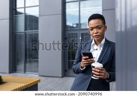 Successful and focused African American business woman uses phone, online during a break with a cup of hot drink