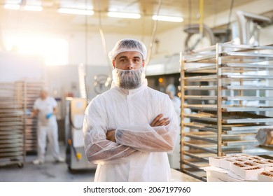 A Successful Food Factory Supervisor In A White Sterile Uniform Is Standing In The Factory With Arms Crossed. He Is Very Satisfied With The Quality And Quantity Of Products.